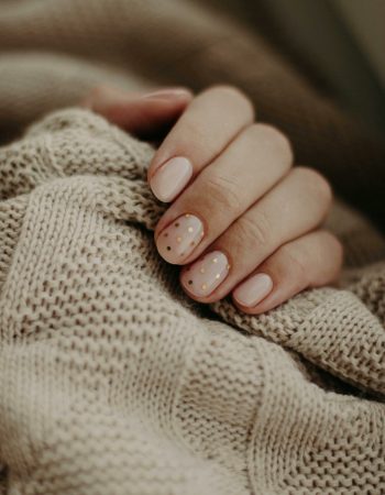 Close-up of a hand with polka dot manicured nails wrapped in a knitted sweater.